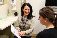 Photo of a smiling doctor showing a document to a patient in an exam room.